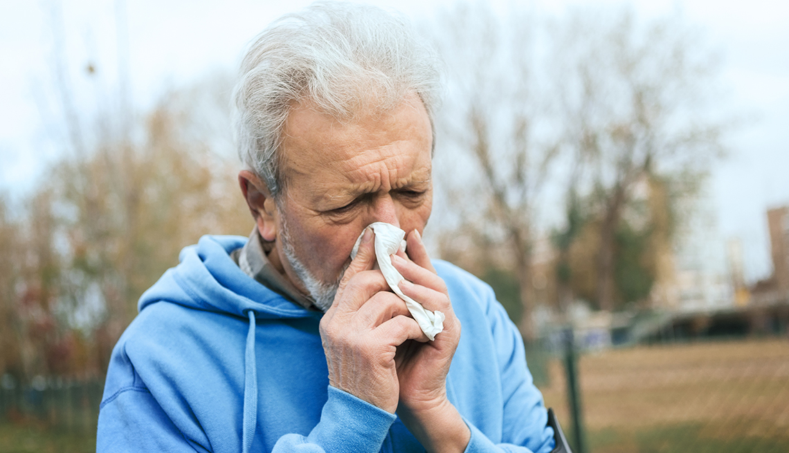 Elderly man in park blowing nose with handkerchief